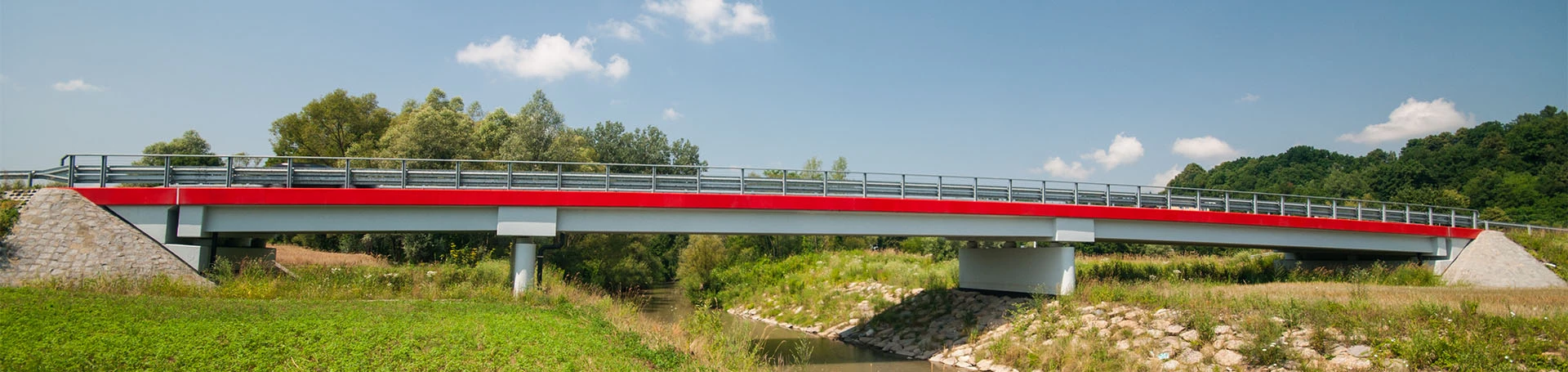 Nowy most nad niewielką rzeka. Brzegi wyłożone kamieniami.